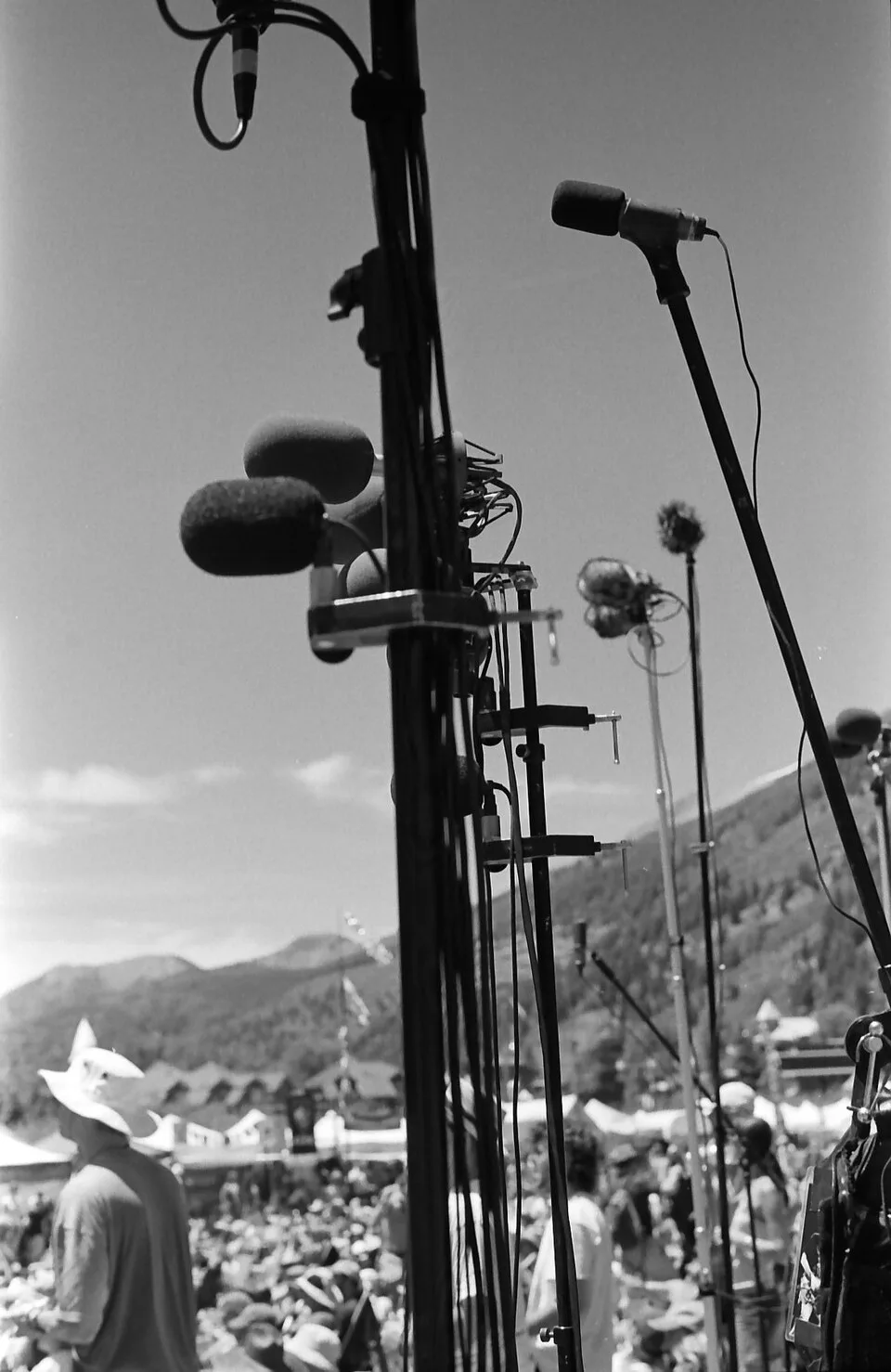 Microphones on tall stands above a festival crowd, with mountains behind